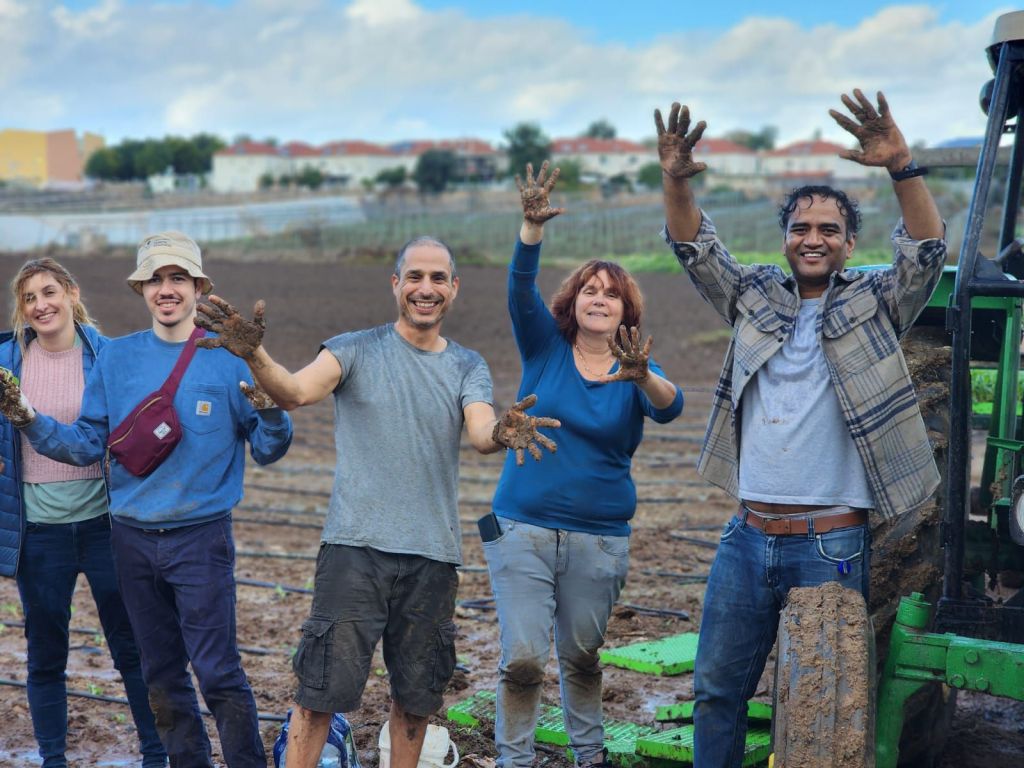 Dr. Amit Agrawal, Prof. Nir Yosef, Dr. Shlomit Zeiger, and Dr. Michal Mark holding up muddy hands during a lab outing. The team from the Systems Immunology Department at the Weizmann Institute of Science was volunteering on a farm.