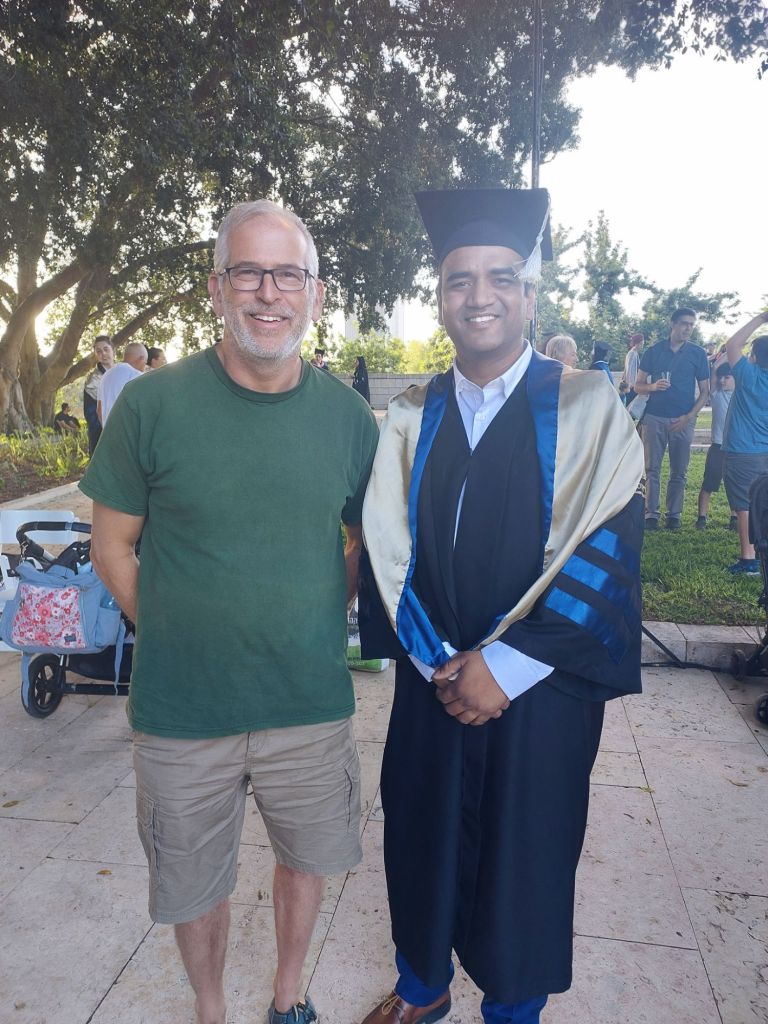 Dr. Amit Agrawal in graduation robes standing with Prof. Uri Alon during the graduation ceremony at the Weizmann Institute of Science, Israel.