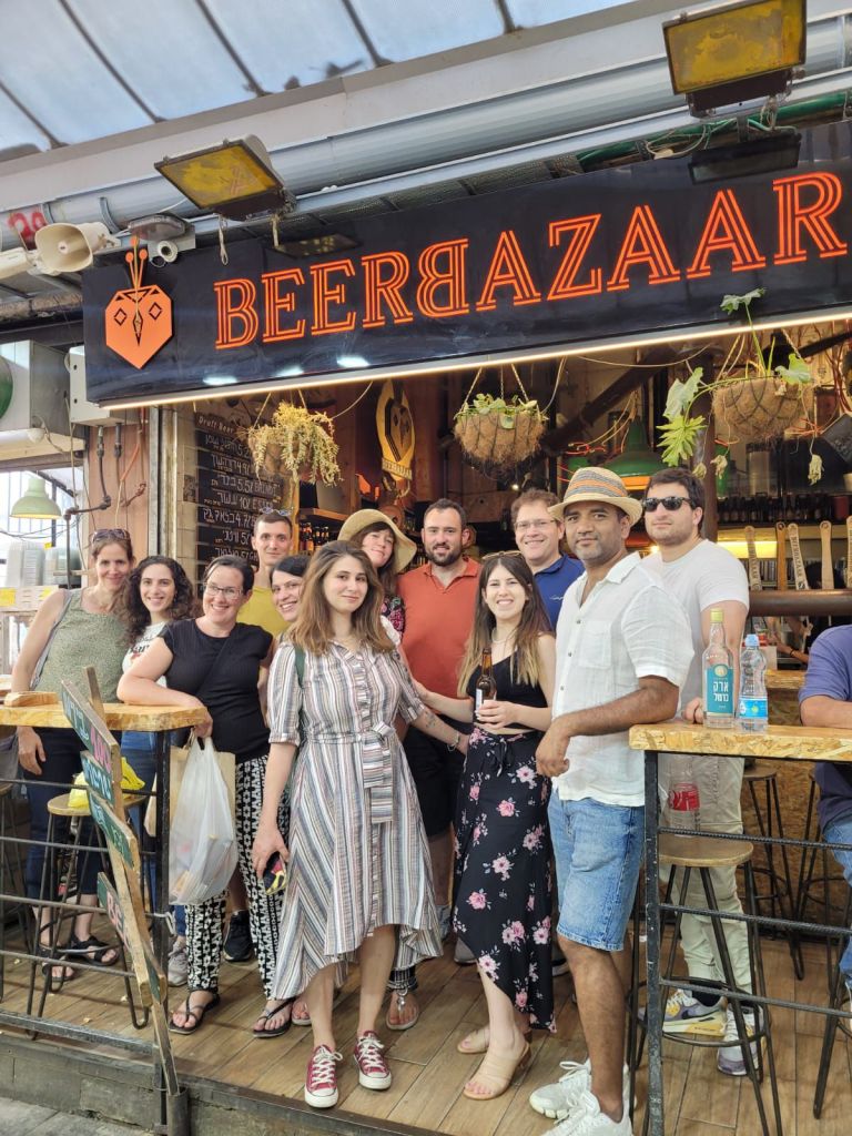 Group photo of Dr. Amit Agrawal with Prof. Valery Krizhanovsky and lab members Dr. Julia Magdalena Majewska, Dr. Noa Cooper, Dr. Riva Shmulevich, Dr. Nurit Levi, Dr. Lior Roitman, and Dr. Nemanja Stanojevic from the Molecular Cell Department at the Weizmann Institute of Science. Photo from a lab outing at Beer Bazaar in Mahane Yehuda Market (shuk), Jerusalem.